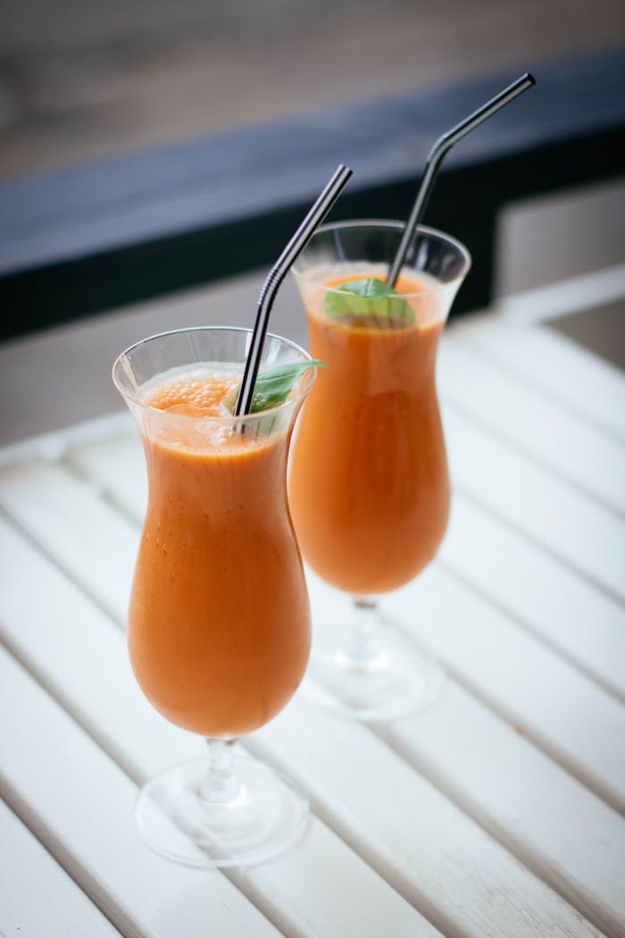 Two tropical smoothies with mint leaves served in tall glasses with straws, perfect for summer.