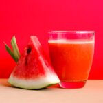 Refreshing watermelon juice and slice against a vibrant red background, perfect for summer vibes.