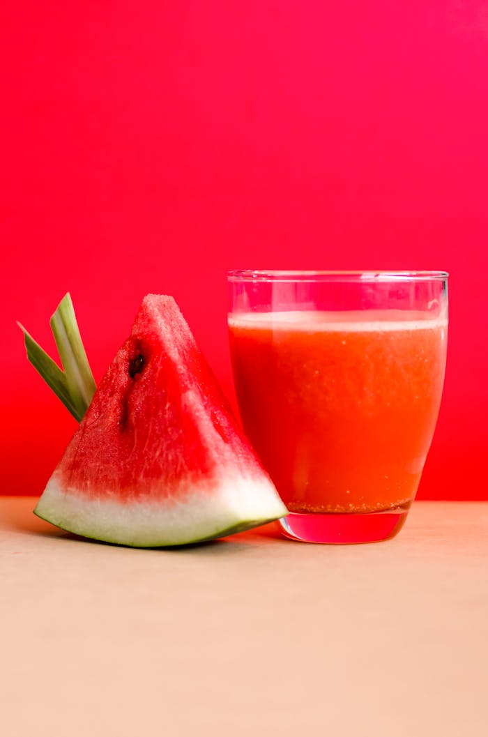 Refreshing watermelon juice and slice against a vibrant red background, perfect for summer vibes.